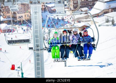 Quatre amis enfants s'assoient sur le télésiège de la montagne avec la pente bondée et la station en dessous Banque D'Images