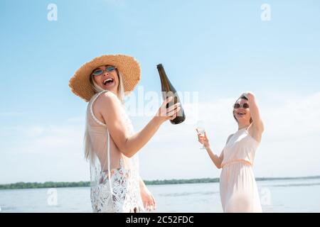 Verser le champagne. Fête saisonnière à la station balnéaire. Femmes, amis au pique-nique, vacances célébrant, se reposer, s'amuser dans la journée ensoleillée d'été. Fêtes, bien-être, vacances, fête. Rire sincère. Banque D'Images