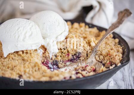 Mûre et bleuet Cobbler cuits dans une poêle en fonte et recouverts d'un gruau doré croustillant à la crème glacée sur une table rustique en bois blanc. Extrema Banque D'Images