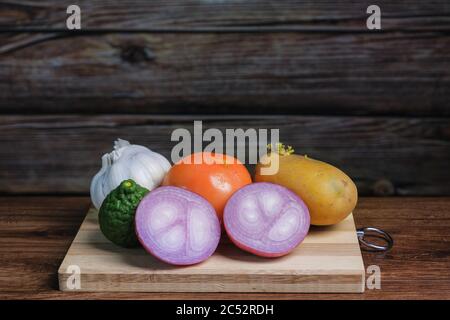 Tomate, ail, calime de kaffir, oignon et pomme de terre sur une planche à découper en bois Banque D'Images