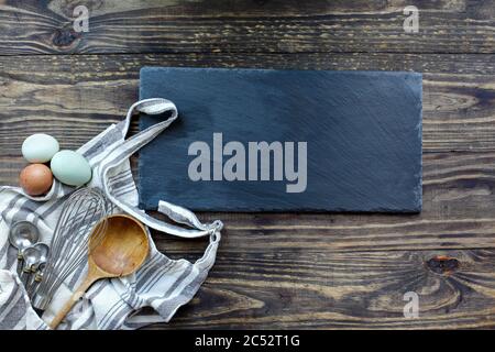 Fournitures de cuisson ou de cuisson avec tablier, fouet, cuillères à mesurer et œufs à côté d'une affiche en ardoise vierge. Image prise depuis la vue de dessus. Banque D'Images