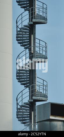 Section d'un escalier métallique en spirale sur un bâtiment industriel contre un ciel bleu Banque D'Images