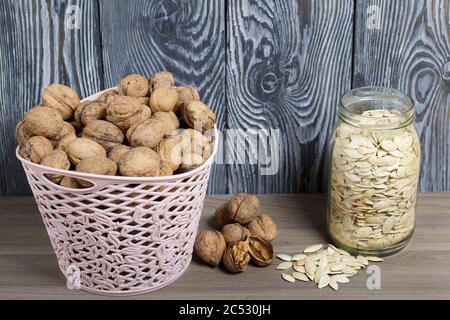 Panier avec noix et une boîte de graines de citrouille. À proximité sont dispersés quelques noix et graines. Sur le fond des planches de pin peintes en noir et Banque D'Images