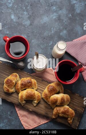 Photo verticale à grand angle de mini croissants sur bois bureau et deux tasses de café rouges Banque D'Images