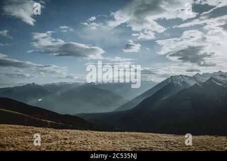 Dernier faisceau de soleil de l'après-midi brillant à travers les sommets enneigés des Alpes italiennes à la vallée de la ville Merano tiré de la prairie jaune au-dessus Banque D'Images