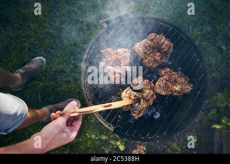 Jeune homme qui a grillé de la viande de poulet sur le barbecue dans le jardin pendant la journée d'été. Banque D'Images