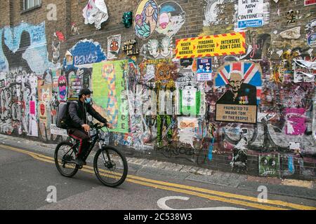 LONDRES, ROYAUME-UNI. 30 juin 2020. Un cycliste portant un masque passe devant un mur avec des affiches satiriques à Brick Lane, dans l'est de Londres, pendant la crise de santé du coronavirus.Credit: amer ghazzal/Alamy Live News Banque D'Images