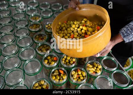 Mains d'un travailleur africain remplissant des pots de verre d'olives vertes marinées dans l'atelier d'emballage de l'usine Banque D'Images