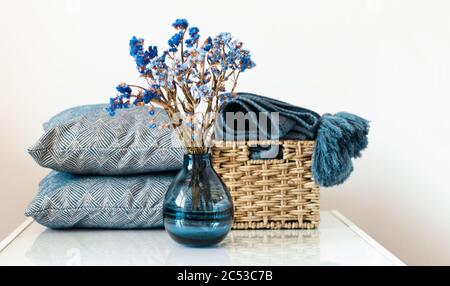 Décoration intérieure chaleureuse : oreiller, tissu écossais, vase bleu avec fleurs sur une étagère blanche dans la chambre. Le concept de quarantaine de rester à la maison Banque D'Images