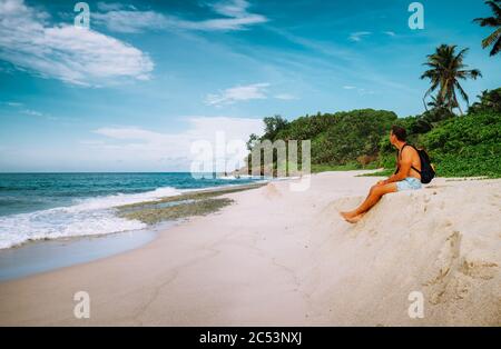 Homme voyageur assis sur le sable profiter de la plage tropicale avec l'océan lagon pendant les vacances. Banque D'Images