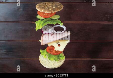 Vue rapprochée d'un sandwich maison avec des ingrédients volants sur fond de bois. Banque D'Images