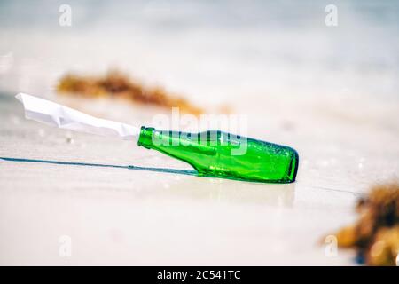 Bouteille verte avec message papier sur la plage de sable blanc. Banque D'Images