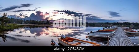 Lever de soleil pendant la lumière de minuit en Laponie suédoise, jetée de mer, beaucoup de bateaux garés, nuages réfléchissent dans l'eau claire et calme. Départ au lever du soleil Banque D'Images