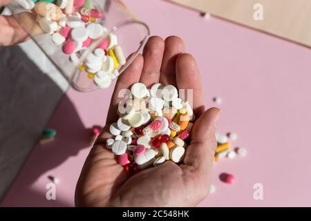 Pilules pharmaceutiques colorées, stupéfiants et vitamines en capsules sur la paume. Verser les capsules d'un verre.espace de copie . homme tenant Banque D'Images