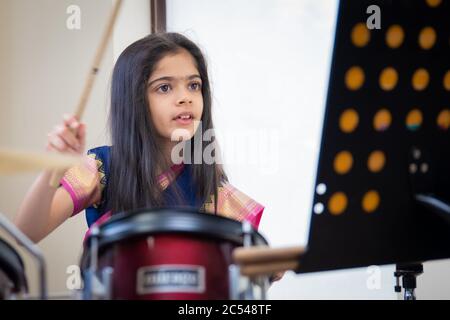 Âge scolaire fille indienne britannique jouant la batterie dans une saree. Banque D'Images