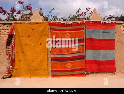 Maroc, Marrakech. Tapis berbères colorés à vendre accrochés sur un mur en adobe sur la route d'Essaouira. Banque D'Images