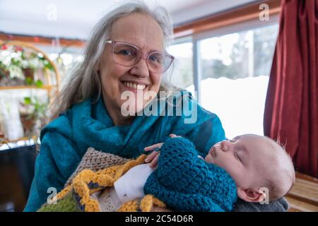 Portrait sélectif de la fière grand-mère tient son petit-fils naissant dans des couvertures tricotées. La famille assemblée dans une cabine du nord. Banque D'Images