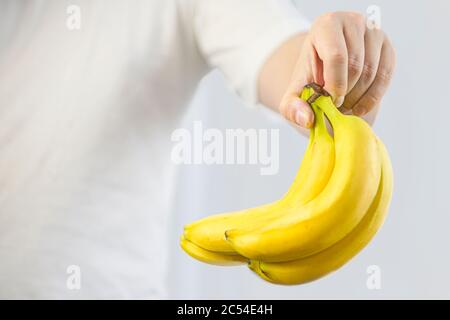 Le gars du T-shirt blanc tient des bananes jaunes dans sa main Banque D'Images