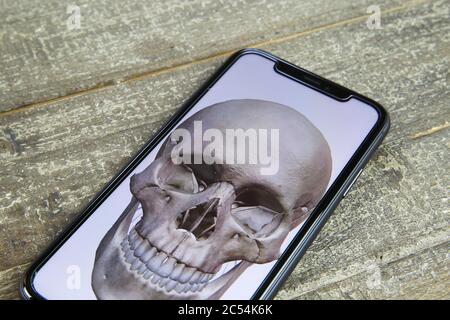 Viersen, Allemagne - juin 30. 2020: Gros plan de l'écran isolé de téléphone mobile avec la peinture du crâne humain sur la table en bois Banque D'Images