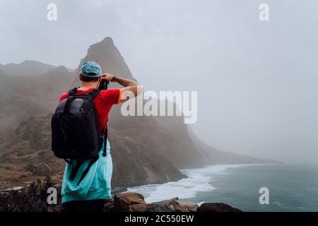 Touriste mâle avec sac à dos sur la route côtière pittoresque. La route mène le long d'immenses falaises volcaniques au-dessus de l'océan de roaring et rejoint les villes de Cruz Banque D'Images