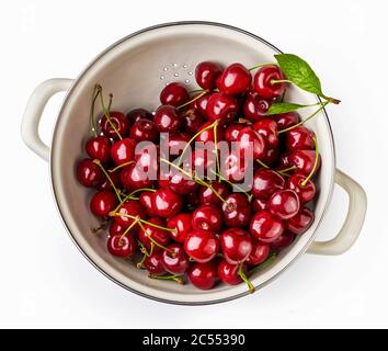 Crépine blanche avec cerises fraîches isolée sur fond blanc. Vue de dessus de la passoire avec baies. Banque D'Images