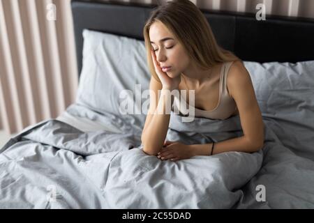 Jeune femme endormi se sentant somnolent ou étourdi après s'être réveillée au lit, souffrant d'un manque de sommeil, d'insomnie, de maux de tête matinaux ou de migraine Banque D'Images