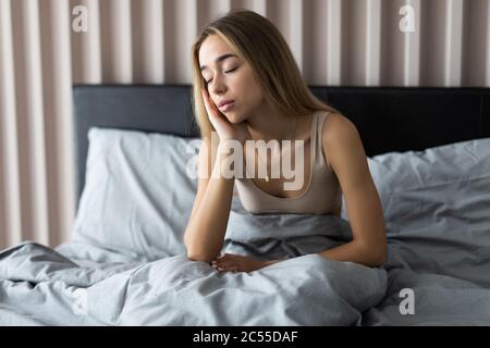 Jeune femme endormi se sentant somnolent ou étourdi après s'être réveillée au lit, souffrant d'un manque de sommeil, d'insomnie, de maux de tête matinaux ou de migraine Banque D'Images