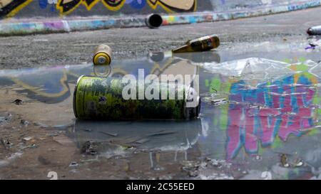 Litière liée aux graffitis sur le sol. Une œuvre d'art se reflète dans une flaque. Montre des bombes aérosol vides et une bouteille de bière. Banque D'Images