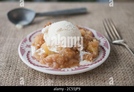 Un morceau de crumble aux pommes maison fraîchement préparé avec de la glace à la vanille sur une assiette rouge. Mise au point sélective avec arrière-plan flou. Banque D'Images