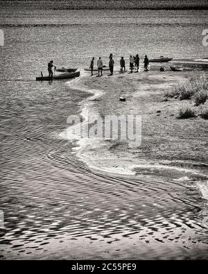 Groupe de personnes sur Riverbank avec petits bateaux Banque D'Images