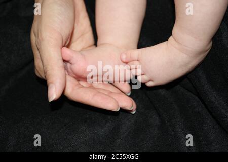 Moment émotionnel de la main de la mère tenant les pieds du bébé sur un fond noir. Banque D'Images