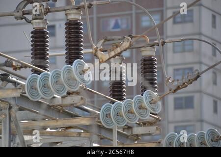 Vue rapprochée des isolateurs en verre et en plastique d'une sous-station de transformateur électrique de ville avec des fils haute tension et un bâtiment en arrière-plan Banque D'Images