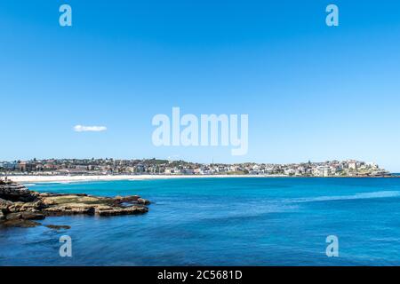 Vue magnifique sur Bondi Beach en été. L'océan est bleu foncé et un seul nuage flotte dans le ciel au-dessus de la ville, de l'autre côté de la baie. Banque D'Images