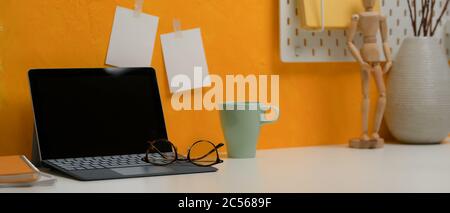 Photo courte d'un espace de travail élégant avec tablette numérique, verres, mug et décorations sur bureau blanc Banque D'Images