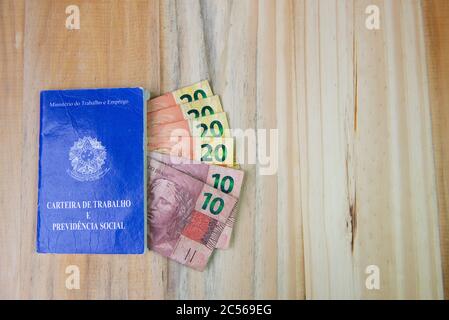 27 juin 2020, Florianopolis - Brésil : vue de dessus du document brésilien de travail et de sécurité sociale et des billets réels sur fond de bois. Concept de pour Banque D'Images