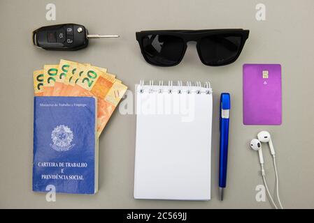 Vue de dessus de la carte de travail brésilienne, billets de banque, clé, lunettes de soleil, stylo, carte de crédit, téléphone à oreilles et téléphone portable sur fond blanc. Traduire: Ministère de la Banque D'Images