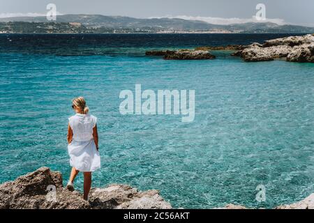 Femme adulte en robe blanche pendant les vacances d'été en profitant du paysage de la côte de la mer de petite plage avec de l'eau bleu limpide. Grèce, Céphalonie. Banque D'Images