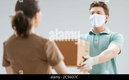 Homme de livraison dans des gants et un masque médicaux en caoutchouc. Achats en ligne. Quarantaine. Femme acceptant des boîtes de messagerie. Banque D'Images