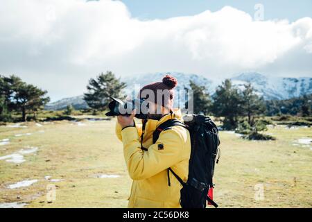 Jeune homme avec veste jaune et sac à dos prenant des photos sur la montagne. Banque D'Images