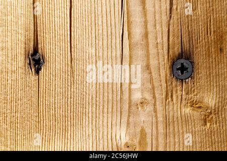 Deux vis noires sont vissées dans un panneau en bois. Banque D'Images
