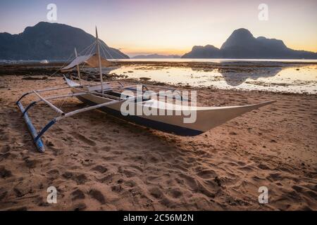 Palawan, Philippines. Plage El Nido avec bateau banca local avec coucher de soleil pittoresque lumière dorée et formes d'île en arrière-plan. Banque D'Images