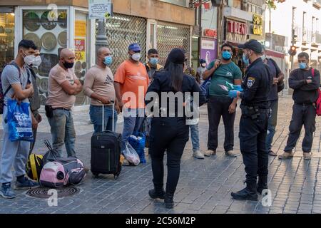 Des policiers israéliens vérifient l'identité des travailleurs palestiniens de la Cisjordanie portant un masque facial en raison de la pandémie du coronavirus COVID-19 qui est venu travailler à Jérusalem dans le centre-ville de Jérusalem-Ouest en Israël. Le gouvernement israélien ne procède pas à des tests de détection du coronavirus pour les travailleurs palestiniens en provenance de Cisjordanie et refuse la demande de l'Autorité palestinienne de tester les travailleurs qui retournent en Cisjordanie. En outre, personne ne surveille les conditions de logement et de travail des 20,000 travailleurs palestiniens qui dorment actuellement en Israël et travaillent à des emplois définis comme « essentiels ». Banque D'Images
