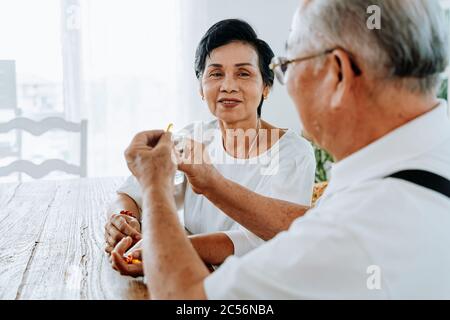Homme asiatique senior et femme prenant des médicaments avec de l'eau le matin à la maison ensemble. Couple de personnes âgées prenant des pilules et se soutenir mutuellement Banque D'Images