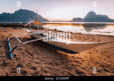 Bateau sur la plage dans la baie d'El Nido. Magnifique paysage avec lagon océanique dans la lumière du coucher du soleil, Palawan, Philippines. Banque D'Images