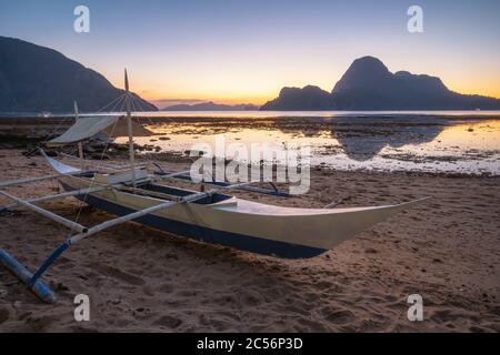 El Nido, Palawan, Philippines. Bateau de pêche traditionnel banca sur la rive. Cadlao Island en lumière du coucher du soleil en arrière-plan. Saison de vacances. Banque D'Images