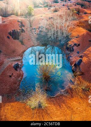 Gant, Hongrie - vue aérienne de la mine de bauxite abandonnée avec petit lac bleu et couleurs chaudes rouge et orange et arbre au coucher du soleil Banque D'Images