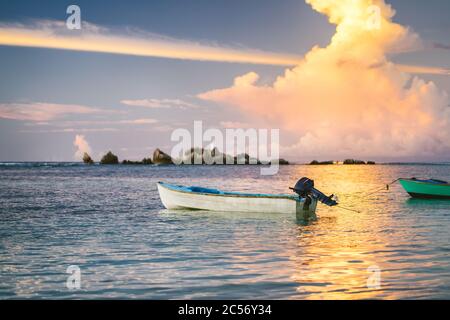 Nuages dorés violets illuminés par le coucher du soleil sur la Digue. Un bateau de pêche flotte dans la baie océanique avec des couleurs de feu à l'horizon. Banque D'Images