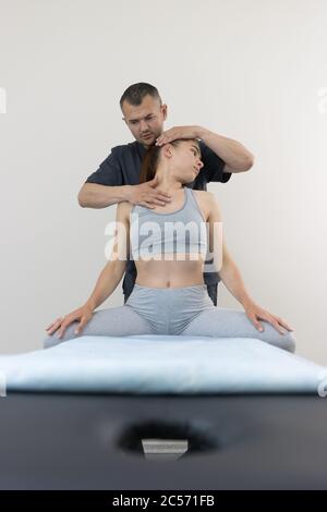 Traitement chiropratique - jeune femme assise sur le canapé et le médecin travaillant avec son cou - tournant la tête sur le côté. Photo intermédiaire Banque D'Images