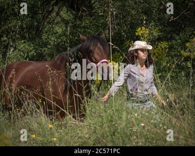 Une cycliste féminine portant un chapeau occidental et sa jument andalouse marchant dans la campagne. Banque D'Images