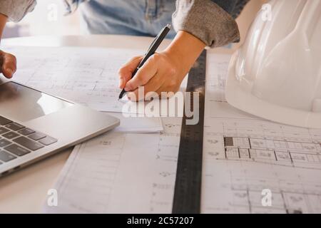 Les ingénieurs tenant un stylo pointant vers un plan de construction de bâtiment et de dessin de dépenses comme guide pour les constructeurs avec des détails.Ingénierie et construction co Banque D'Images